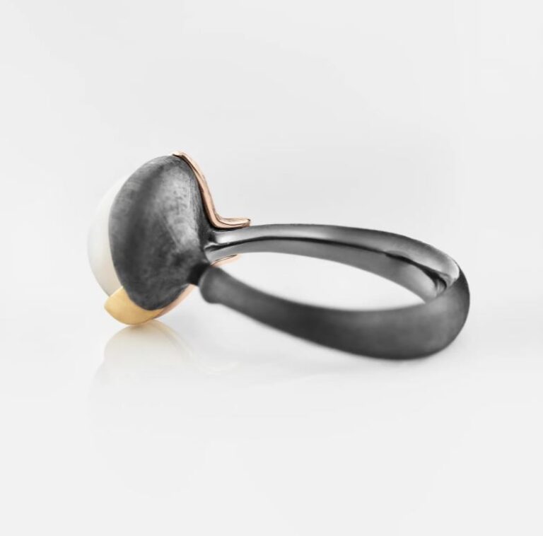 Lotus ring i mix av sølv og gull. I midten er det fattet en hvit cabochonslipt månesten, fra Ole Lynggaard