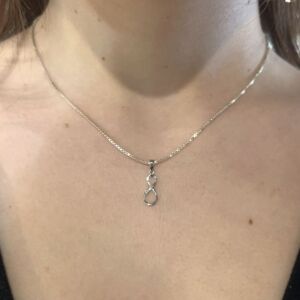 Anheng i hvitt gull med evighetstegn. PÅ den ene buen er det fattet små diamanter. Her er det på halsen til en modell.