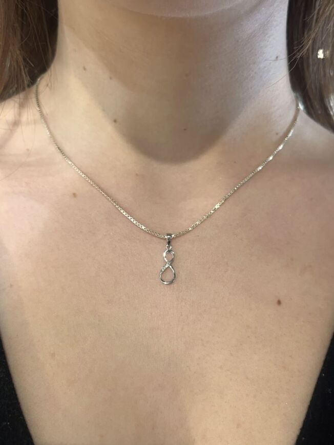 Anheng i hvitt gull med evighetstegn. PÅ den ene buen er det fattet små diamanter. Her er det på halsen til en modell.