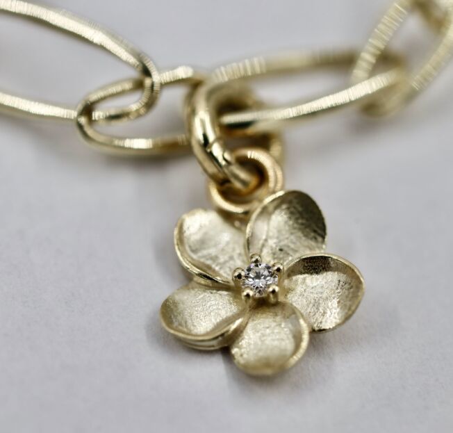 Blomsterserien til EC 1914 laget i Sandnes gult gull. Enkelt armbånd med åpne ringer med avtagbar blomstercharms med diamant i midten.