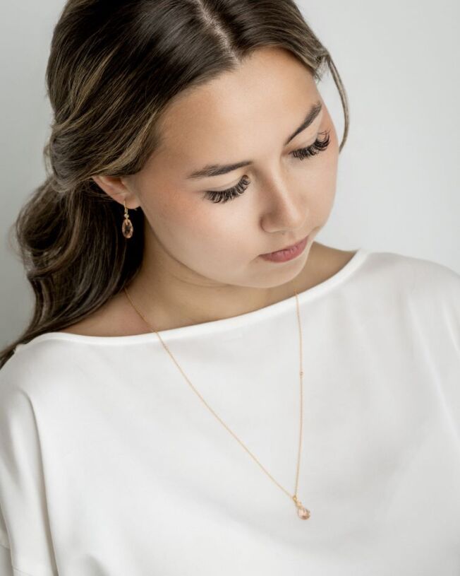Ofelia ørepynt i forgylt sølv med krystall som er fasettslipt i en krok med en oval c.zirkonia som er fattet over. Fargen kalles Peach, Ferskenfarget. I tillegg anheng på kjede med krystall.